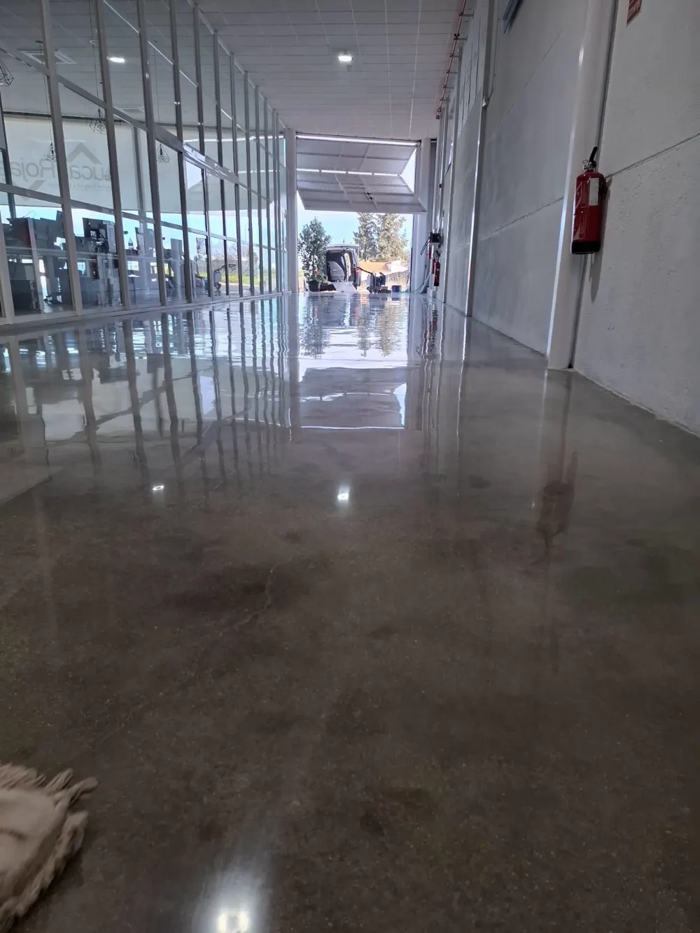 Pasillo de nave con reflejos, cristalera y furgoneta al fondo — trabajo real de Pulimentos Jiménez